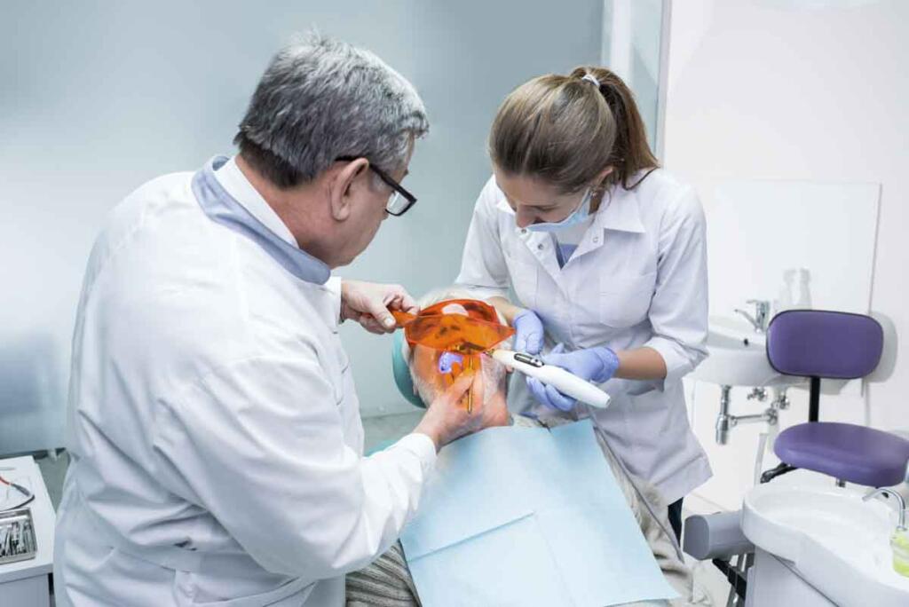 Dental doctor using ultraviolet light. Senior patient and two dentists. Wide spectrum of medical services.