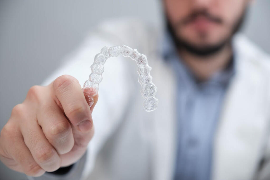 Unrecognizable young orthodontist holding invisible dental aligners.