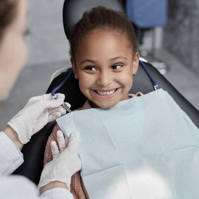 Smiling little girl in dental chair with nurse preparing her for teeth check up